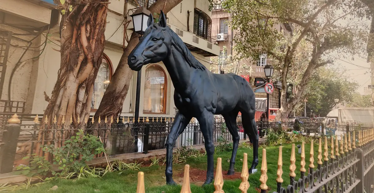 Black horse statue as public art on a grassy area in an urban street setting.