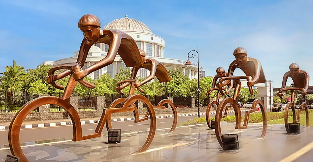 Bronze sculptures of cyclists in motion, part of a public art installation on a city street, representing sports and activity.