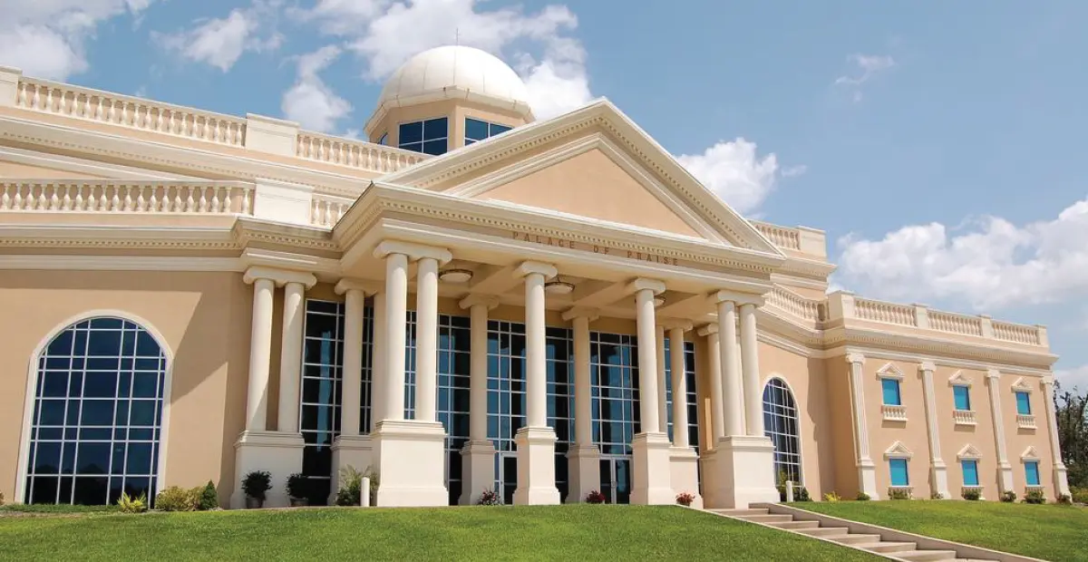 The grand neoclassical 'Palace of Praise' building with stately columns and a domed roof, set against a bright sky.