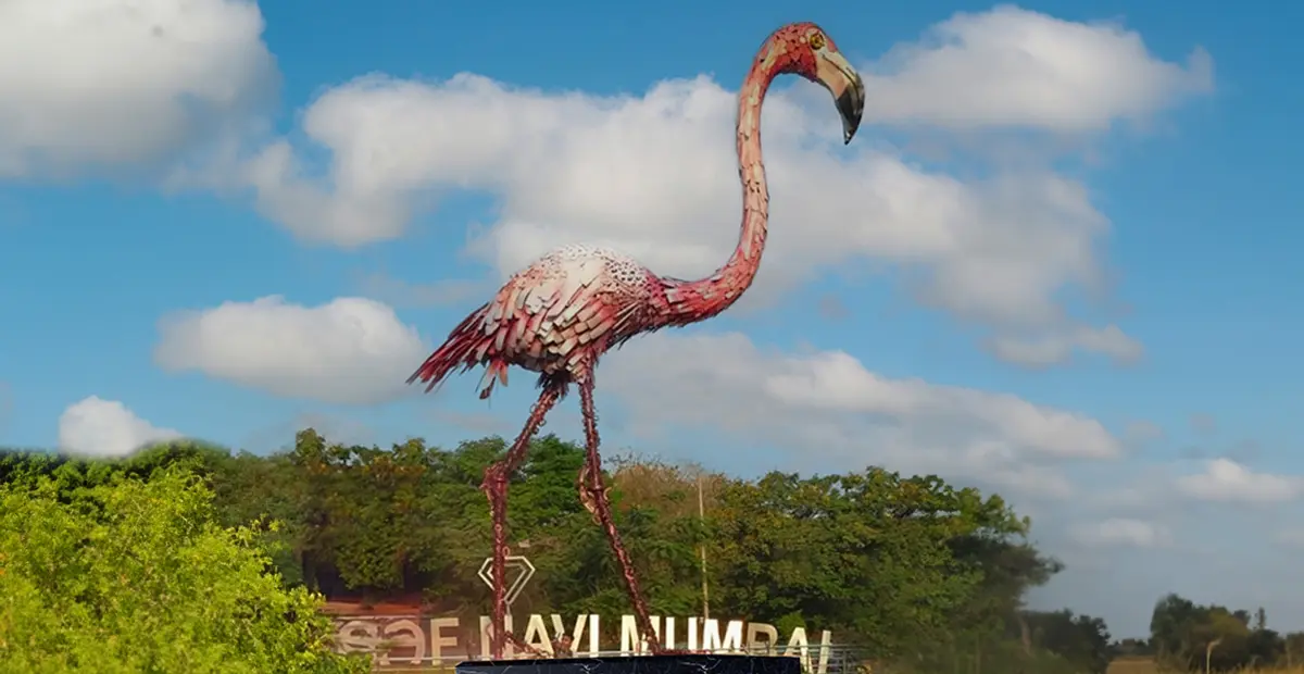 Enormous pink flamingo statue, a landmark public art piece, with a clear sky and 'Navi Mumbai' sign in the background.